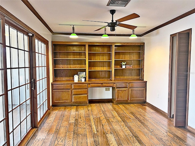 unfurnished office with crown molding, ceiling fan, built in desk, and light hardwood / wood-style flooring