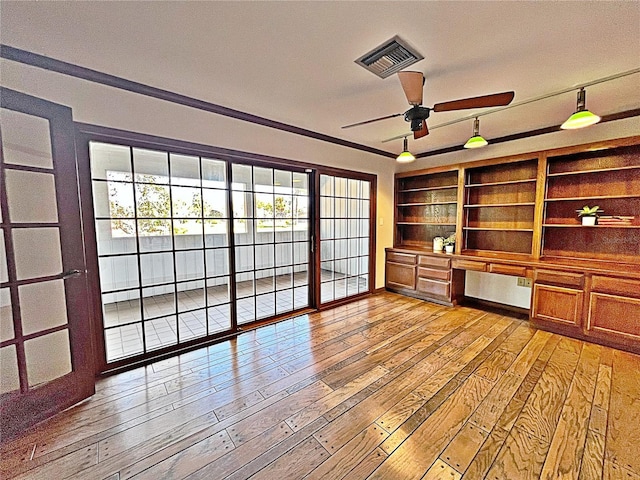 interior space featuring built in shelves, built in desk, ceiling fan, and light hardwood / wood-style flooring