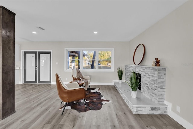 living area with a brick fireplace, light hardwood / wood-style flooring, and french doors