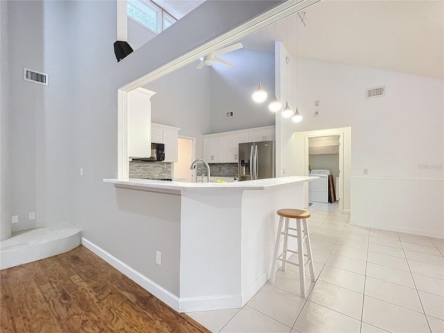 kitchen with stainless steel fridge, a breakfast bar area, white cabinetry, washer / dryer, and kitchen peninsula