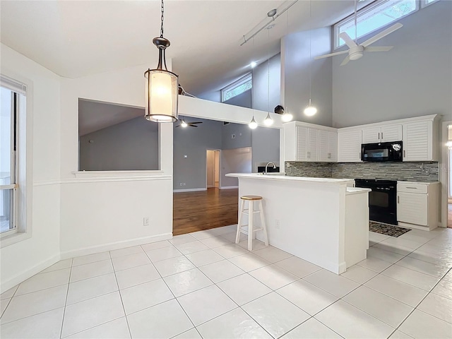 kitchen featuring a breakfast bar area, white cabinetry, light tile patterned floors, kitchen peninsula, and black appliances