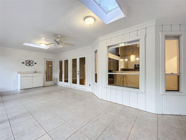 tiled empty room featuring sink, crown molding, a skylight, and ceiling fan