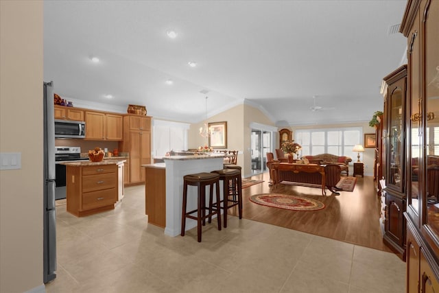 kitchen with lofted ceiling, a breakfast bar, decorative light fixtures, a center island, and appliances with stainless steel finishes