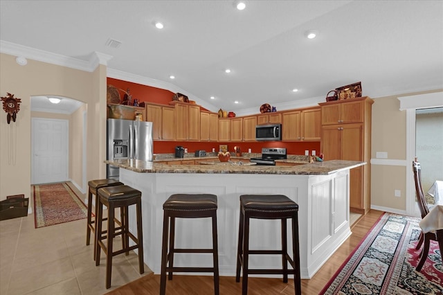 kitchen with ornamental molding, appliances with stainless steel finishes, a kitchen bar, and a kitchen island with sink