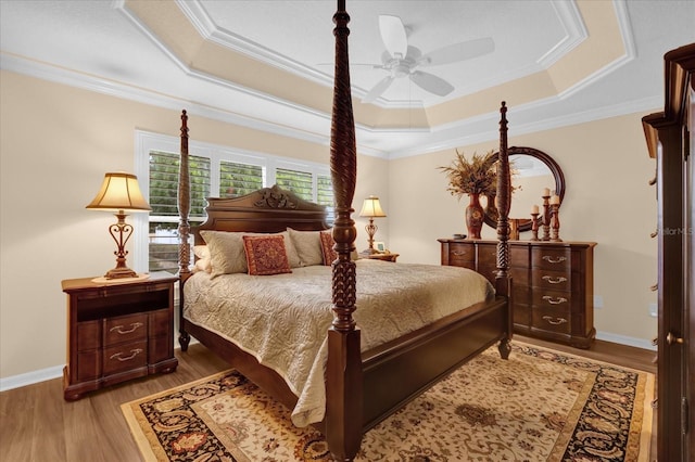 bedroom with ceiling fan, ornamental molding, a raised ceiling, and light hardwood / wood-style flooring