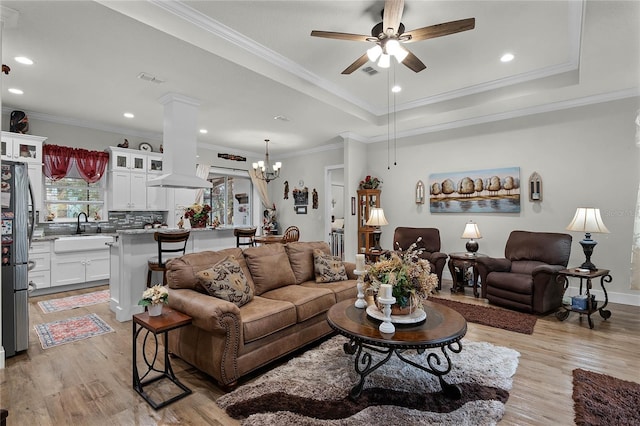 living room featuring sink, light hardwood / wood-style flooring, ceiling fan with notable chandelier, a raised ceiling, and ornate columns