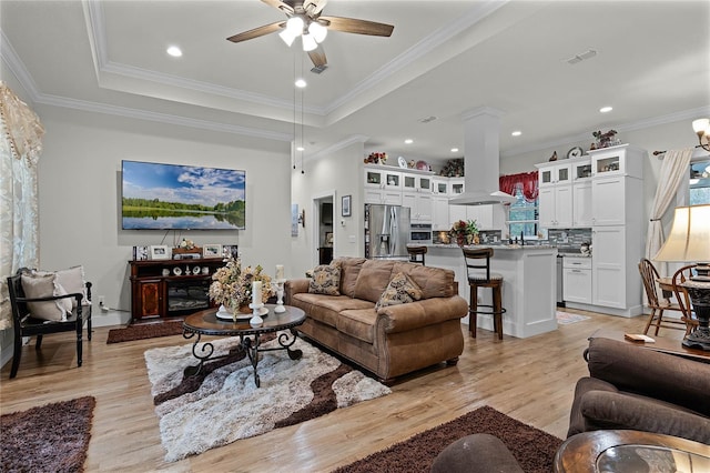 living room with ceiling fan, a tray ceiling, and light wood-type flooring