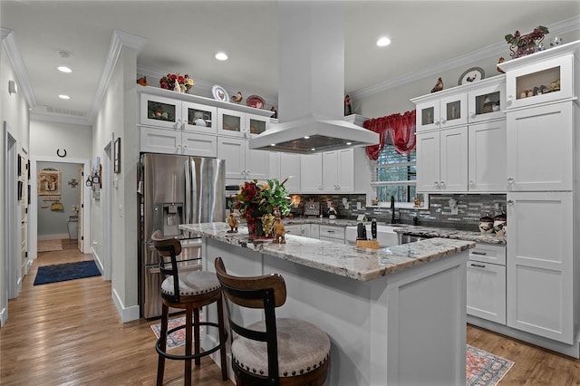 kitchen featuring stainless steel fridge, a kitchen breakfast bar, island range hood, white cabinets, and a kitchen island