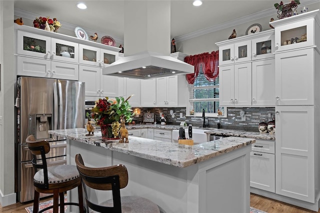 kitchen with stainless steel refrigerator with ice dispenser, light stone counters, island range hood, a kitchen island, and white cabinets