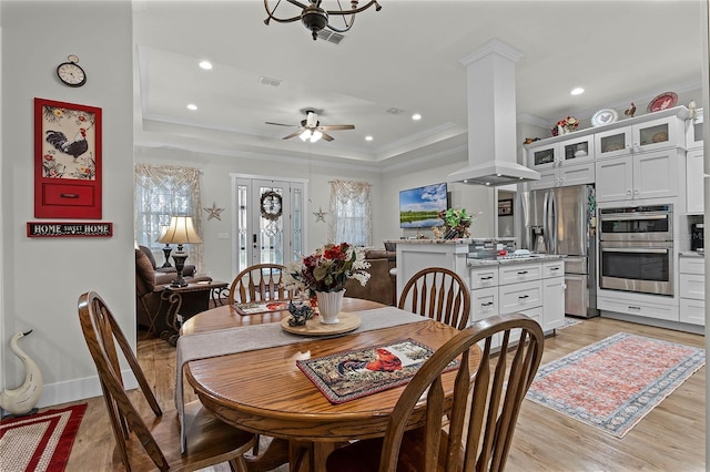 dining room with ornate columns, ceiling fan, a raised ceiling, crown molding, and light hardwood / wood-style flooring