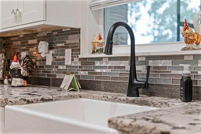 details with tasteful backsplash, light stone countertops, sink, and white cabinets