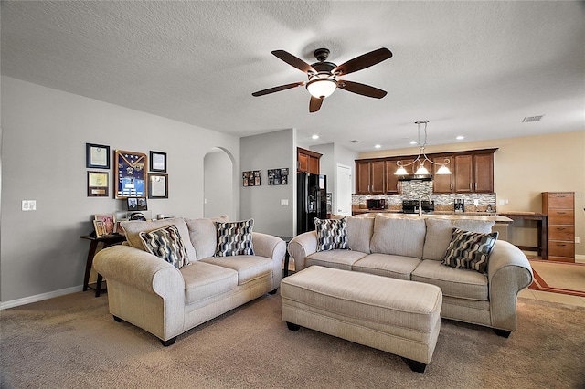 carpeted living room featuring sink, ceiling fan with notable chandelier, and a textured ceiling