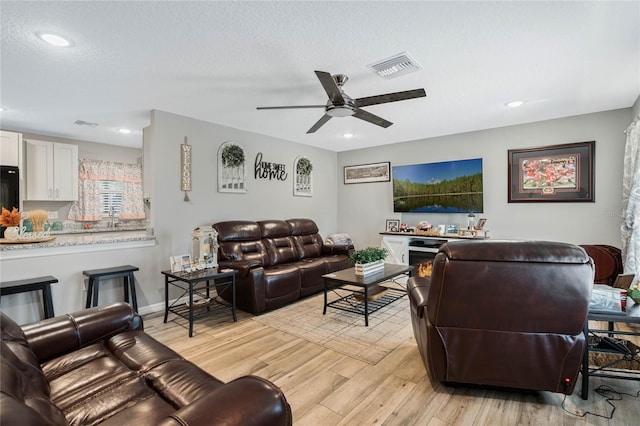 living room featuring ceiling fan, light hardwood / wood-style flooring, and a textured ceiling