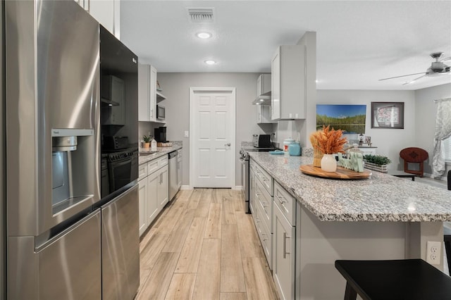 kitchen with white cabinetry, light wood-type flooring, light stone countertops, and appliances with stainless steel finishes