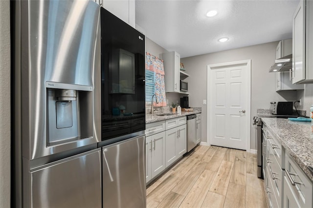 kitchen with sink, light hardwood / wood-style flooring, stainless steel appliances, light stone countertops, and exhaust hood