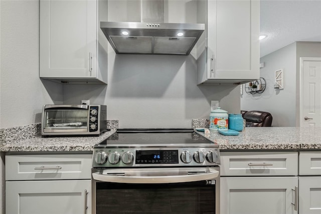 kitchen featuring white cabinetry, wall chimney exhaust hood, light stone countertops, and stainless steel electric range