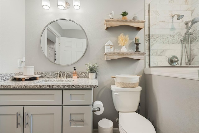 bathroom featuring vanity, a tile shower, and toilet