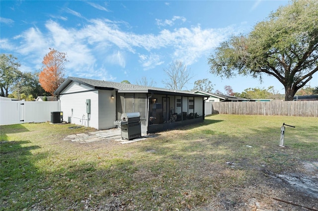 rear view of property with a sunroom, central AC, and a lawn