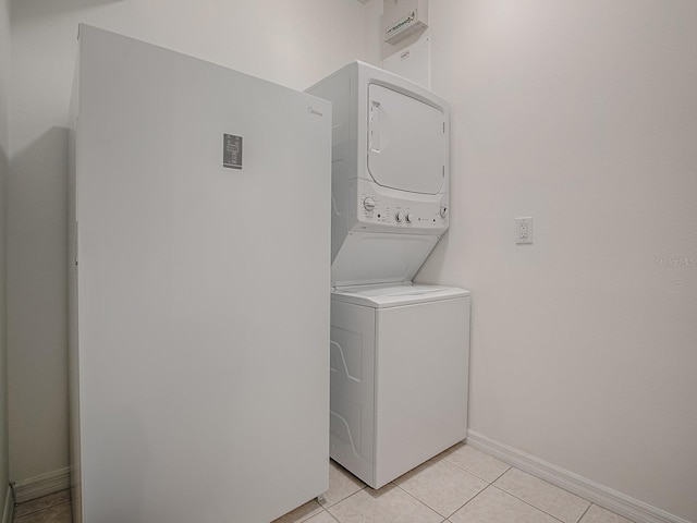 clothes washing area featuring stacked washer and dryer, laundry area, baseboards, and light tile patterned flooring