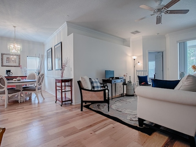 living area featuring a textured ceiling, ceiling fan with notable chandelier, light wood-type flooring, and visible vents