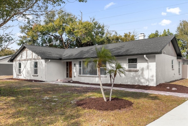 view of front facade featuring roof with shingles, a front lawn, a chimney, and stucco siding