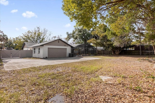 view of yard featuring a garage, concrete driveway, glass enclosure, a fenced backyard, and a gate