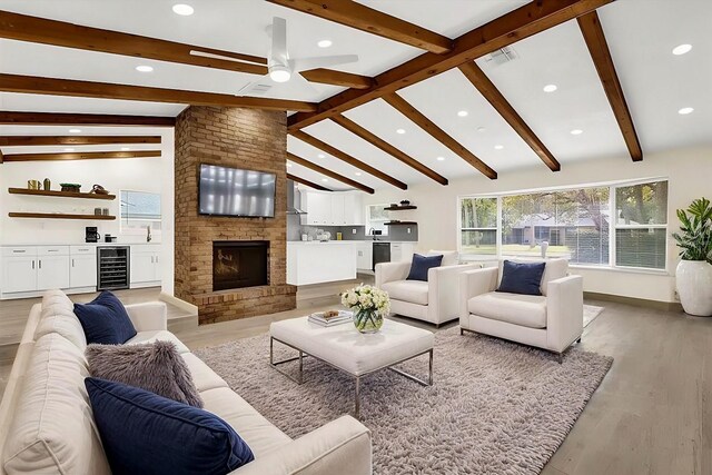 living room featuring lofted ceiling with beams, wine cooler, visible vents, light wood-style floors, and a brick fireplace