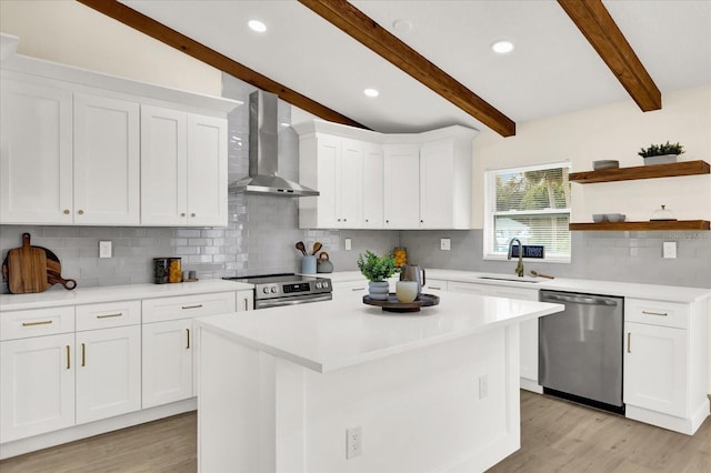 kitchen featuring appliances with stainless steel finishes, white cabinetry, a sink, and wall chimney exhaust hood