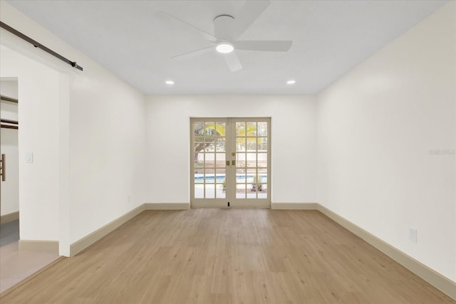 unfurnished room with a barn door, baseboards, french doors, light wood-type flooring, and recessed lighting