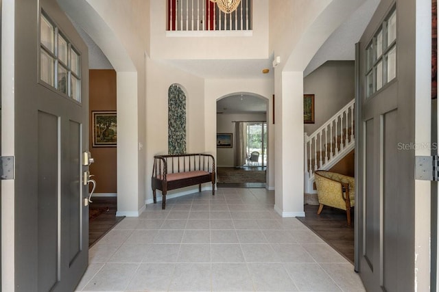 entryway with a towering ceiling, baseboards, stairway, and light tile patterned flooring