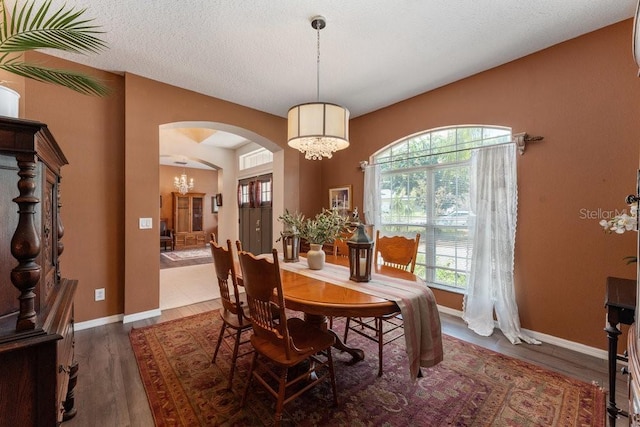 dining room with dark wood-style floors, arched walkways, an inviting chandelier, a textured ceiling, and baseboards