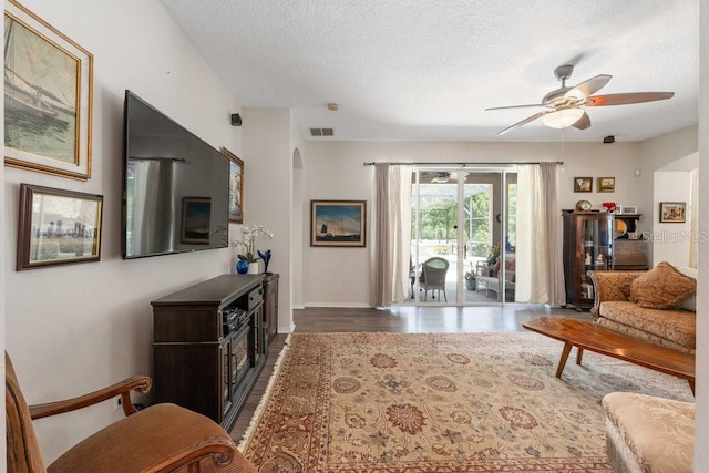 living area featuring dark wood-style floors, arched walkways, visible vents, a ceiling fan, and a textured ceiling