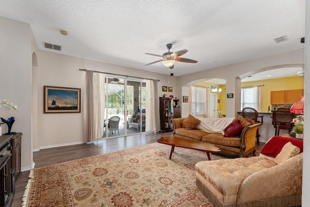 living room with arched walkways, dark wood-style flooring, visible vents, and a textured ceiling