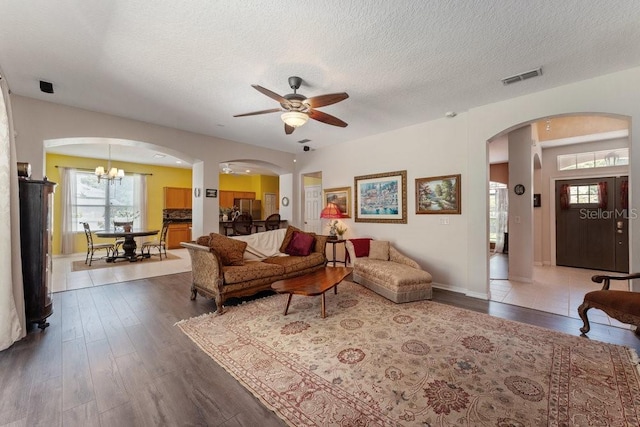 living room featuring visible vents, arched walkways, dark wood-style flooring, a textured ceiling, and a notable chandelier