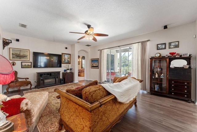 living area featuring visible vents, arched walkways, a glass covered fireplace, dark wood-style floors, and a textured ceiling