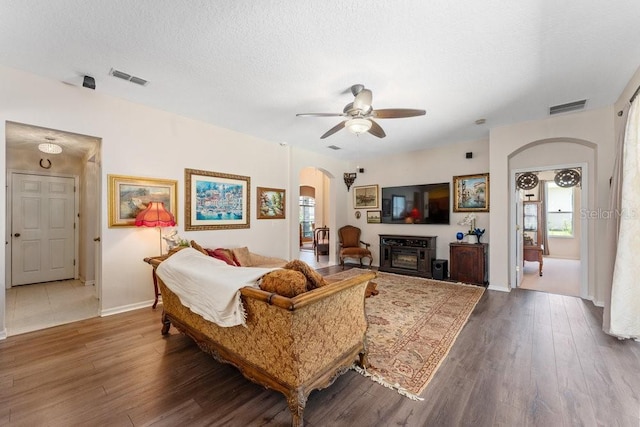 living area with arched walkways, visible vents, dark wood finished floors, and a textured ceiling