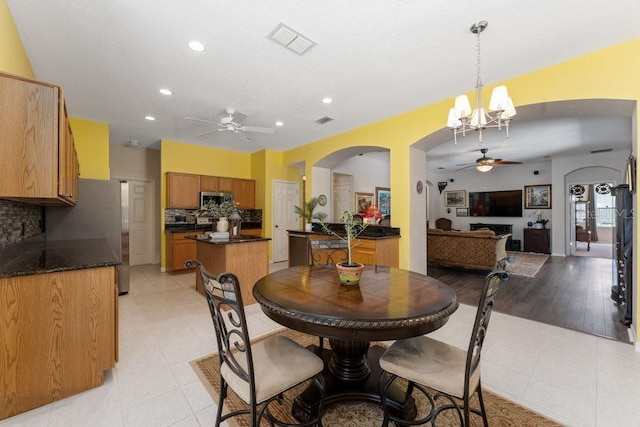 dining space featuring arched walkways, light tile patterned floors, ceiling fan with notable chandelier, and visible vents