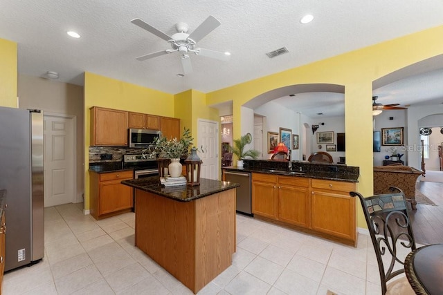 kitchen featuring stainless steel appliances, visible vents, a sink, dark stone countertops, and a peninsula