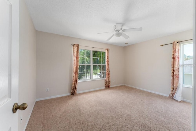 spare room featuring light carpet, a textured ceiling, baseboards, and a healthy amount of sunlight