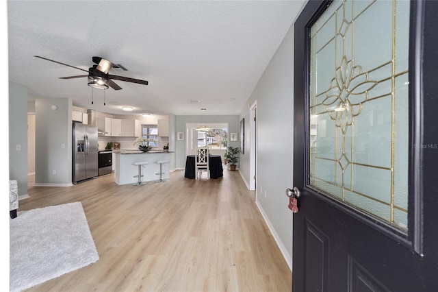 entryway with ceiling fan, a textured ceiling, and light wood-type flooring