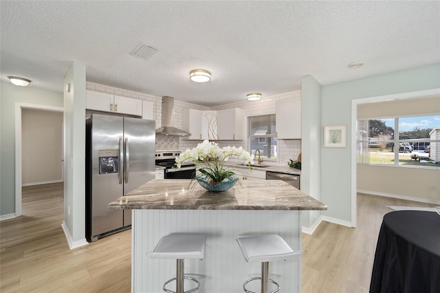 kitchen featuring white cabinets, a kitchen breakfast bar, a center island, stainless steel appliances, and wall chimney exhaust hood