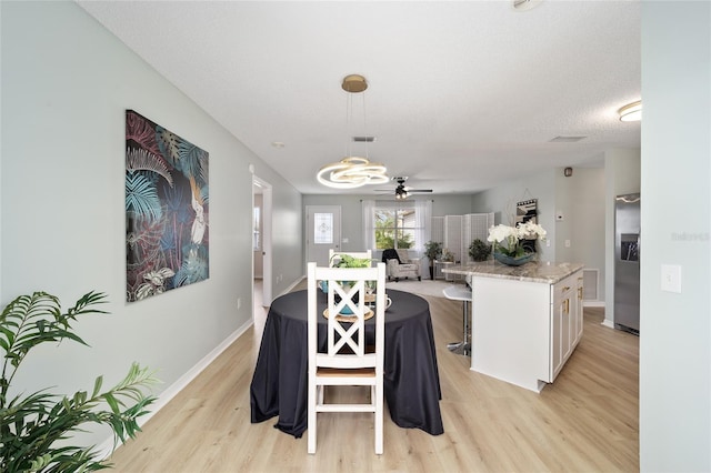 kitchen featuring stainless steel refrigerator with ice dispenser, light stone countertops, white cabinets, a kitchen island, and decorative light fixtures