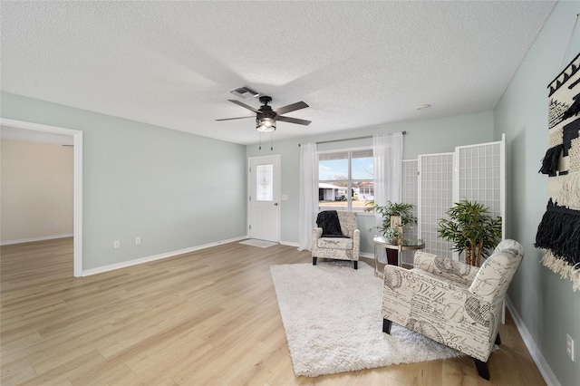 living area with ceiling fan, wood-type flooring, and a textured ceiling