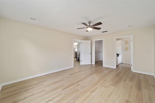 unfurnished bedroom with a spacious closet, a textured ceiling, light wood-type flooring, a closet, and ceiling fan