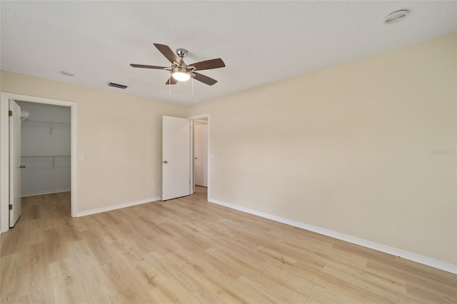 unfurnished bedroom with light hardwood / wood-style flooring, ceiling fan, a textured ceiling, a walk in closet, and a closet