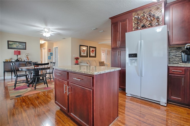 kitchen featuring backsplash, wood-type flooring, white fridge with ice dispenser, and a center island