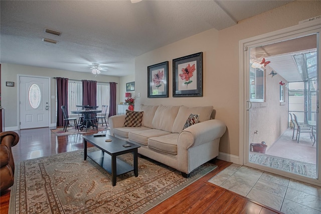 living room with ceiling fan, a textured ceiling, and light wood-type flooring