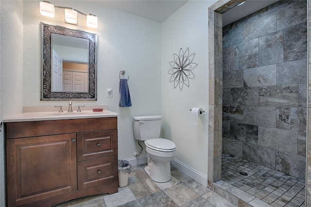 bathroom with a tile shower, vanity, and toilet