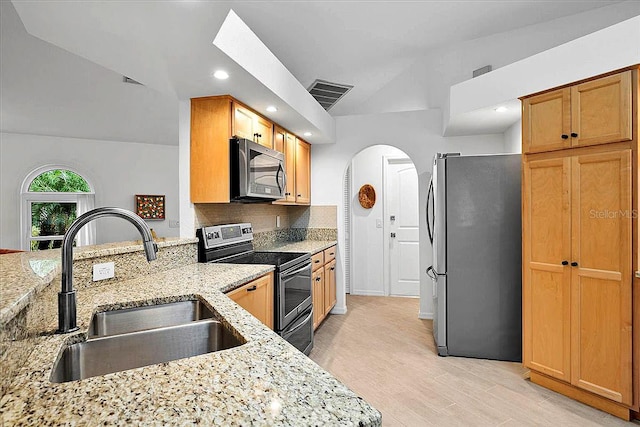 kitchen with vaulted ceiling, appliances with stainless steel finishes, sink, decorative backsplash, and light stone counters