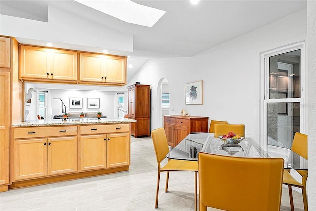 kitchen with light brown cabinets, light wood-type flooring, vaulted ceiling with skylight, and light stone counters